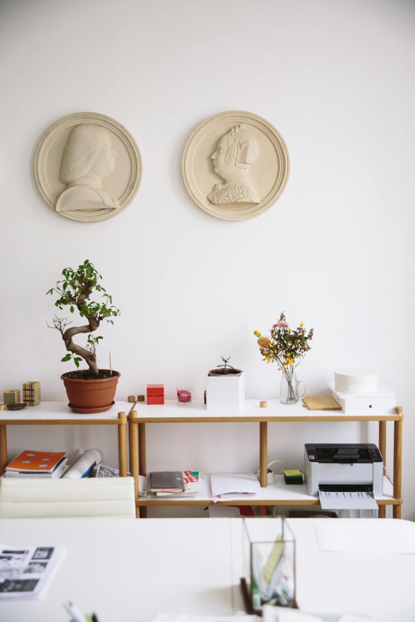 Sveikas bonsų medelis ant palangės, su išlaikyta miniatiūrine forma ir prižiūrėtais lapais.